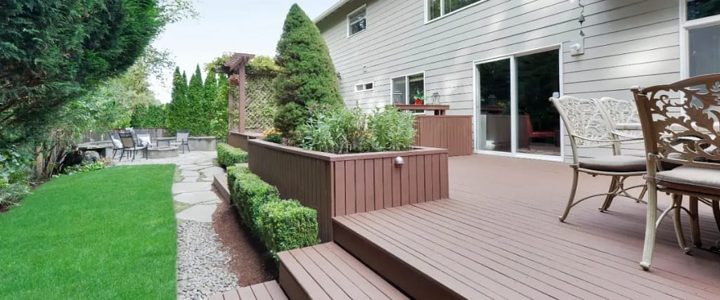 A composite deck featuring a table and chairs set up in a sunny backyard.