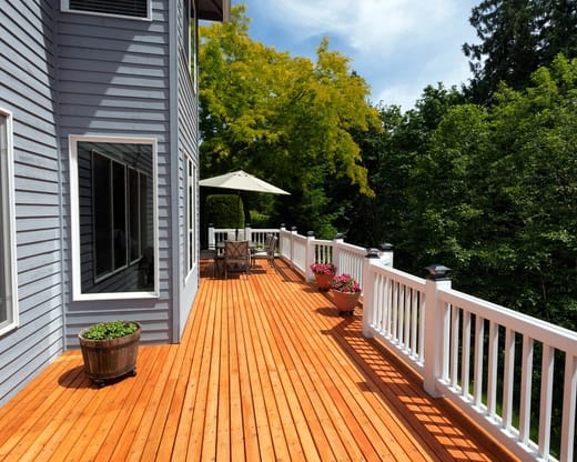 A large, newly built wooden deck with a bright orange stain, white railings, and a patio dining set with an umbrella.