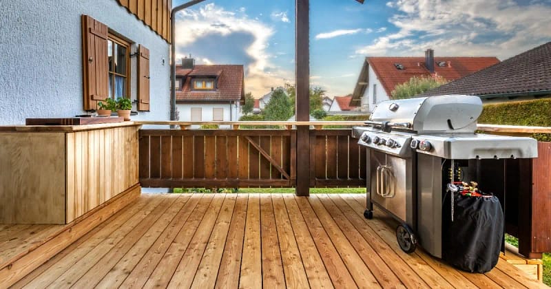 A grill on a cedar deck beside a wooden table, creating a cozy outdoor cooking space.